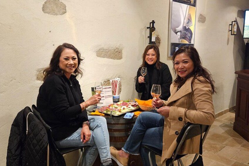 Three people seated at a table with food and drinks, in a room with stone walls and a poster. 2