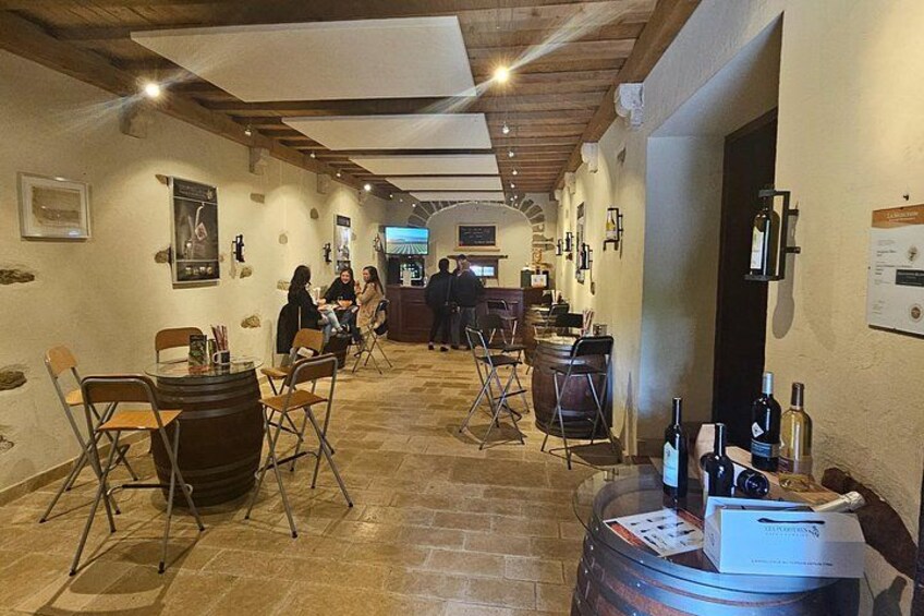 A wine cellar with wooden barrels, a bar area, and people socializing. 3