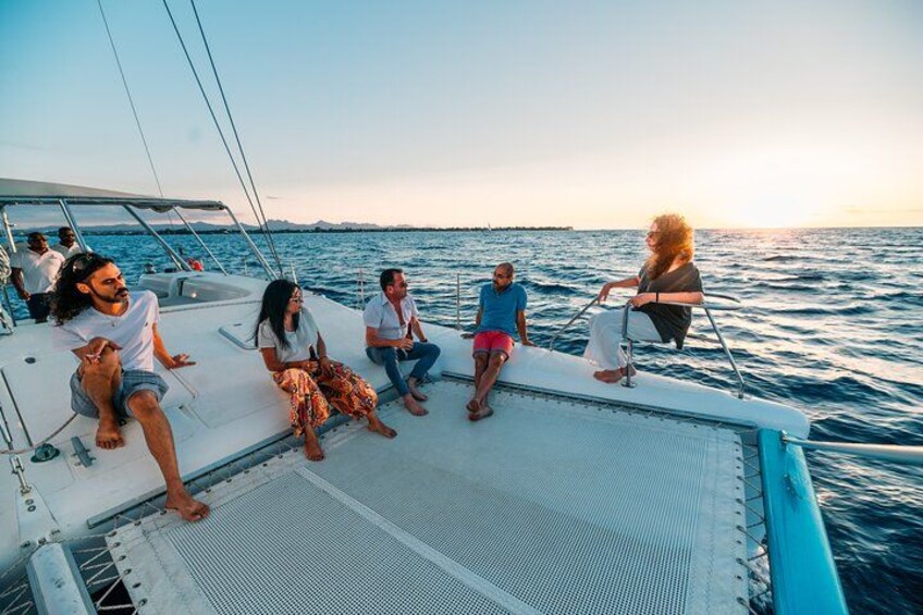 En gruppe mennesker på en sejlbåd med oceanen og en solnedgang i baggrunden. 5