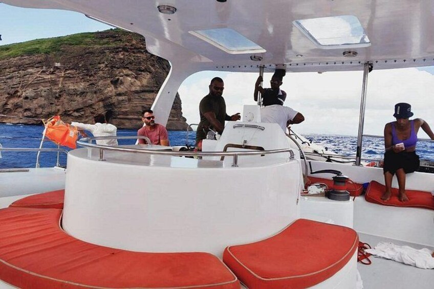 Un bateau à l’intérieur blanc et aux coussins rouges, des personnes sur le pont et, en arrière-plan, une côte rocheuse. 3