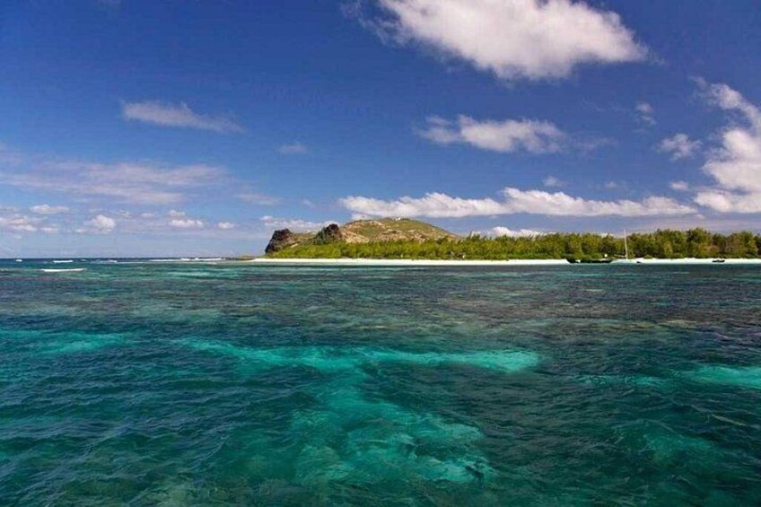 A clear blue sea with a small island and rocky outcrops in the distance. 3