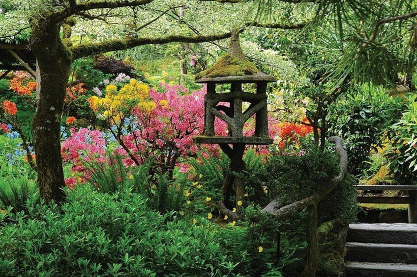 A garden with a wooden lantern, colorful flowering trees, and a stone staircase. 2