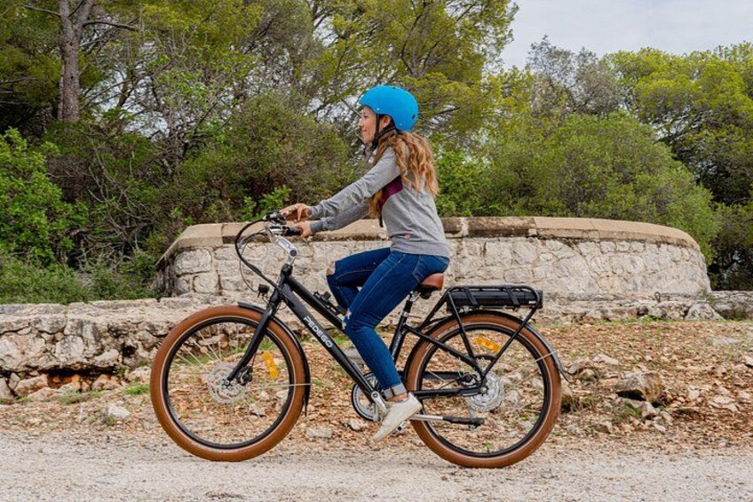 A person riding a bicycle on a gravel path with a stone wall and trees in the background. 1