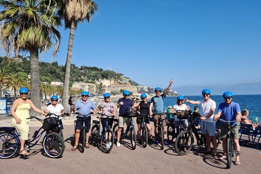 Een groep mensen met fietshelmen die op een promenade aan zee staan. 1
