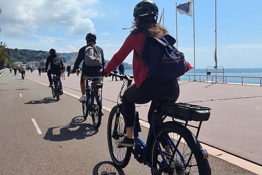 A coastal bike path with cyclists, a clear sky, and a flag on a pole. 5