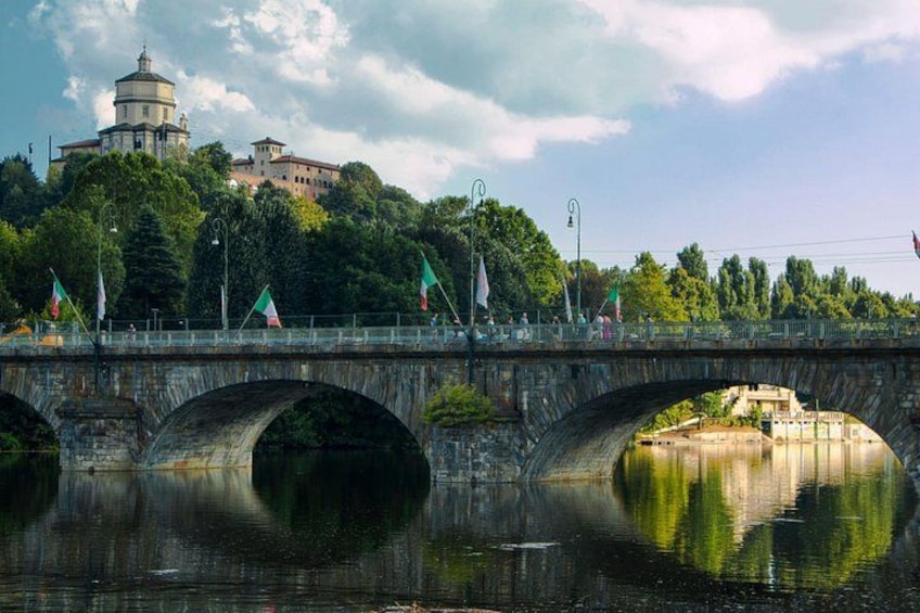 Un puente de piedra con tres arcos sobre un río tranquilo, reflejando la vegetación circundante y un edificio distante. 3