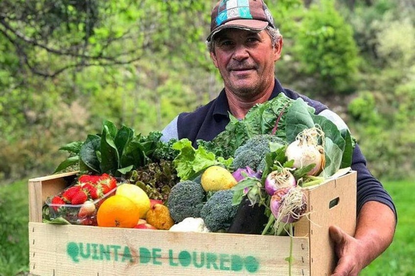 A man holding a wooden crate filled with various vegetables. 4