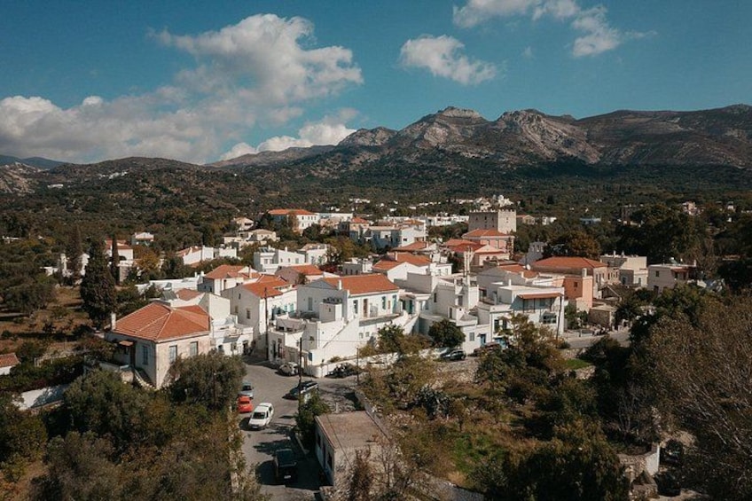 Un pueblo costero con edificios blancos y techos rojos, rodeado de montañas y vegetación. 3