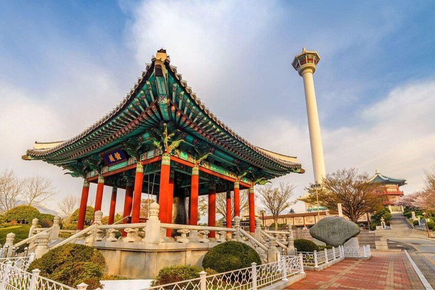 Ein traditioneller chinesischer Pavillon mit rotem Dach und grünen Überh ängen, eine weiße, säulenförmige Struktur und ein hoher weißer Turm im Hintergrund. 1