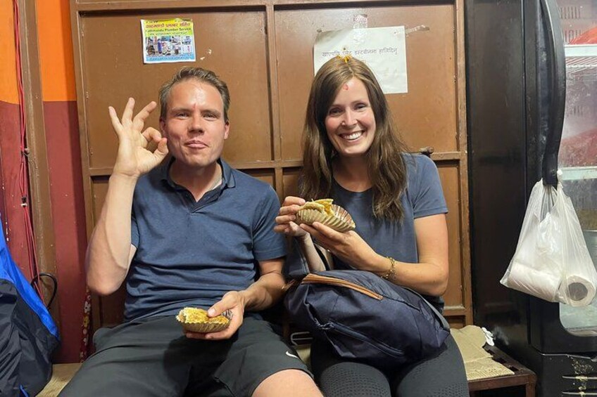 Two people sitting on a bench, one holding a snack. 3