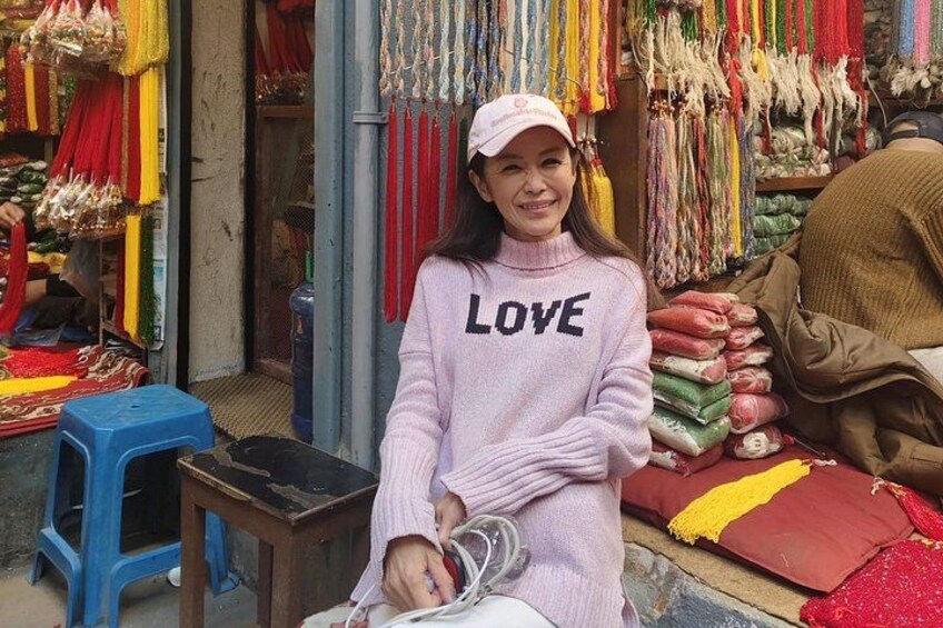 A person sitting at a market stall with colorful textiles and bags in the background. 3