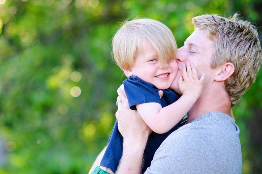 A person holding a child in an outdoor setting with greenery in the background. 3