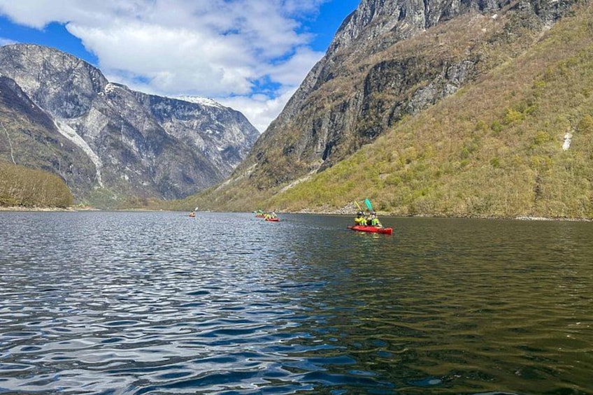 A calm lake with a red kayak and a small boat in the distance, surrounded by mountains. 2