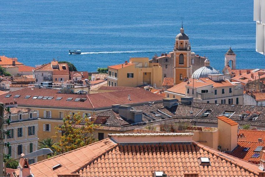 Paesaggio costiero con edifici a tetti in terracotta, una chiesa importante con una cupola e una barca sul mare. 5