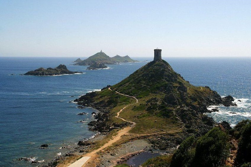 Paesaggio costiero con una collina imponente, una torre e un sentiero che conduce al mare. 3
