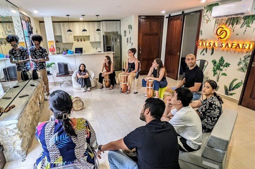 A group of people sitting in a circle in a modern indoor setting with a 'Salsa Safari' sign. 1