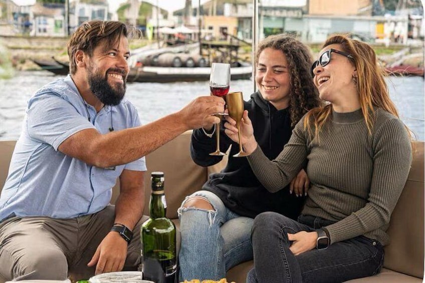 Un gruppo di persone brinda con calici di vino su una barca, con un fiume e degli edifici sullo sfondo. 5