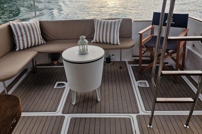 Een dek van een boot met een zitzone met kussens, een klein rond tafeltje en een stoel. 4