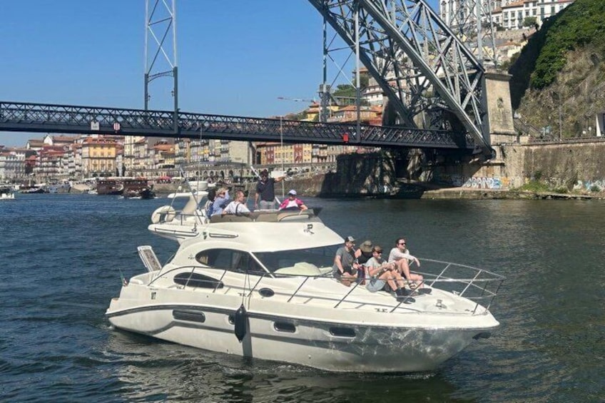 Eine weiße Yacht mit Passagieren auf einem Fluss, mit einer Brücke und Gebäuden im Hintergrund. 2