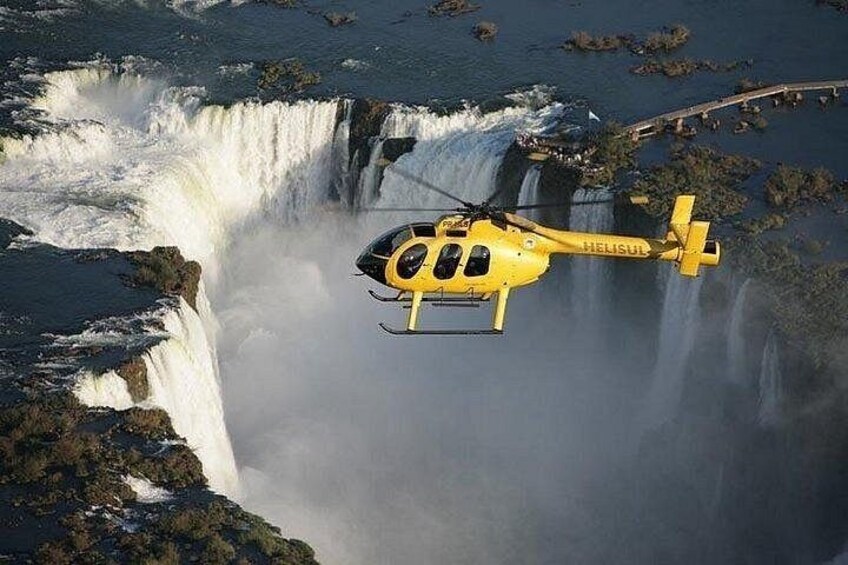 A yellow helicopter flying over a waterfall. 3