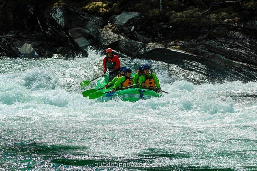 Een groep mensen in een groene raft die door een stroomversnelling met wit water navigeert. 2