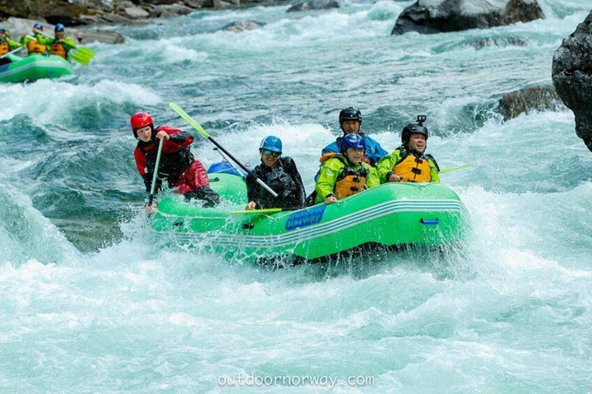Een groep mensen in een groene opblaasbaar rubberboot die door een rivier met stromingen peddelt. 1