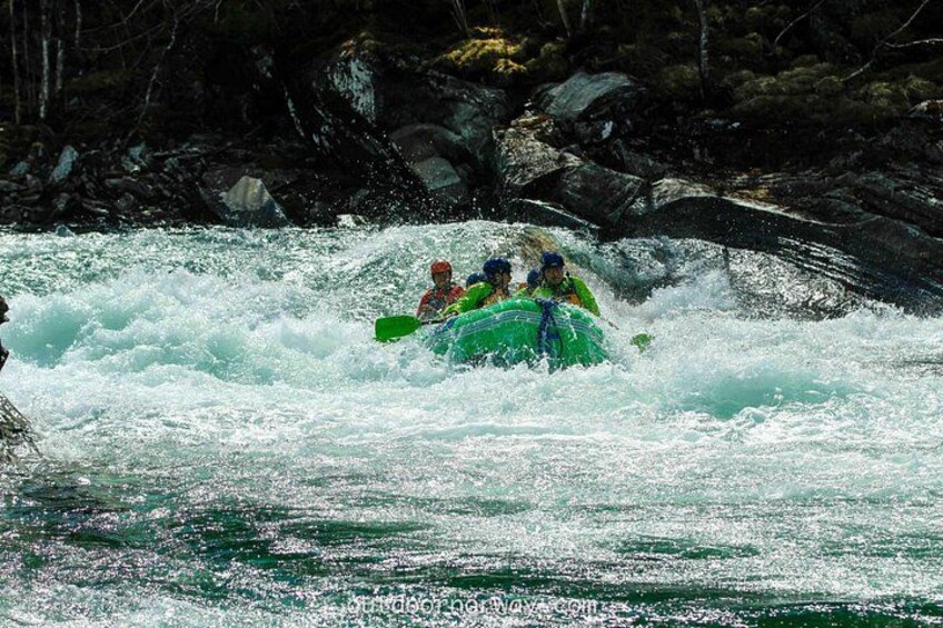 Een groep mensen in een groene raft die door witte waterrapids navigeert. 3