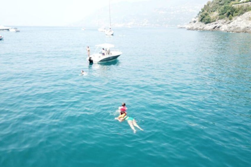 A person swimming in a body of water with boats and a rocky coastline in the background. 4