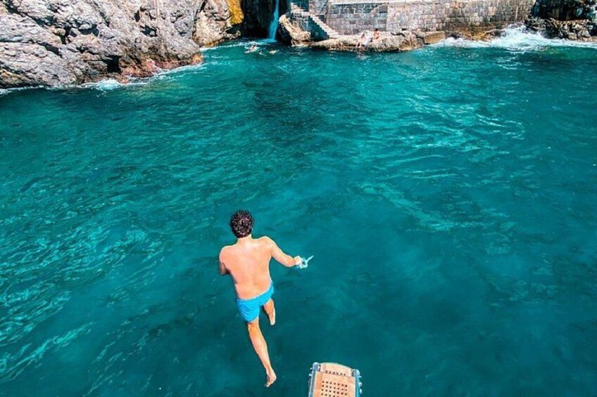 A person swimming in clear blue water with a rocky shore and a waterfall in the background. 2