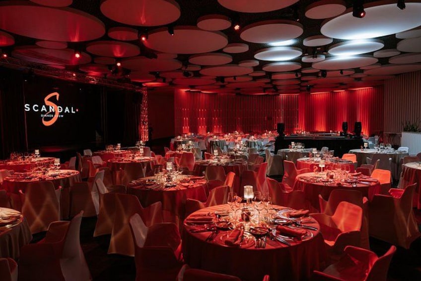 A banquet hall with round tables, red chairs, and a stage with a red curtain backdrop. 5