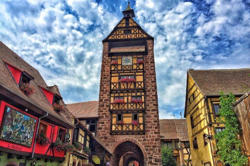 Un edificio tradizionale a graticcio con una torre dell'orologio, circondato da case colorate e un cielo sereno. 1