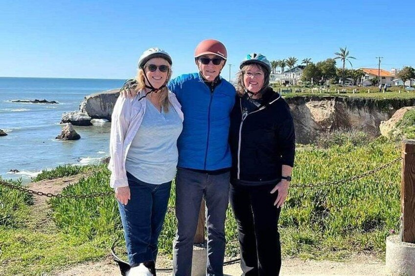 Three people standing on a path near a coastal area with a view of the ocean and rocky cliffs. 5