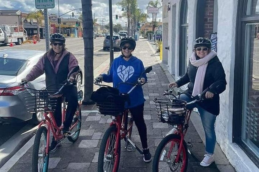 Three people on bicycles on a sidewalk with buildings and a car in the background. 3