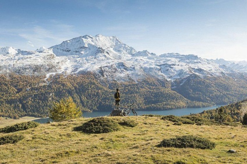 Una persona in piedi su una collina erbosa, con una catena montuosa e un lago sullo sfondo. 1