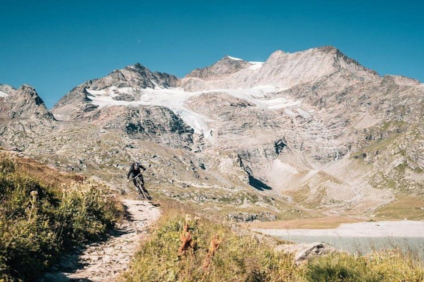 Un ciclista da montagna su un sentiero roccioso, con un ghiacciaio sullo sfondo. 4
