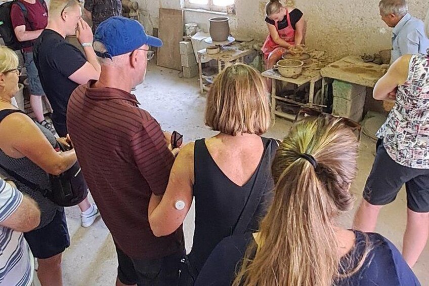 A group of people observing an activity in a rustic setting with wooden tables and tools. 2