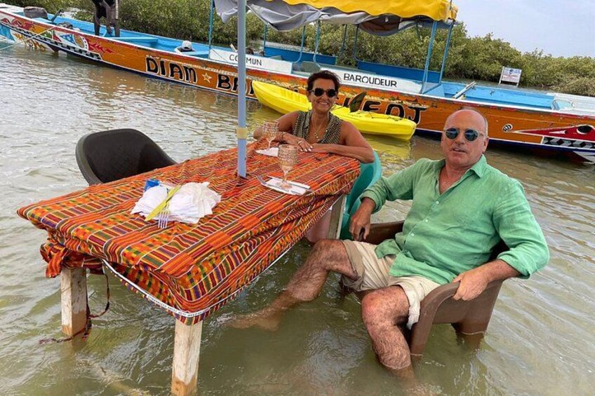 Two people sitting at a table on a boat in a body of water, with other boats in the background. 3
