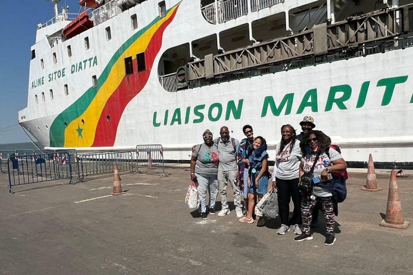 A group of people posing in front of a large ship named 'Liaison Maritime' with a colorful design on its side. 1