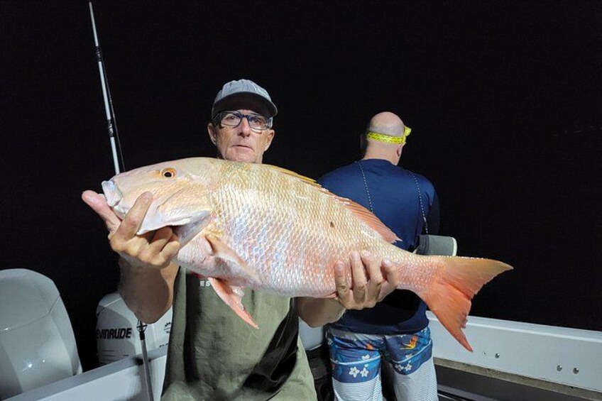 A person holding a large fish, wearing a cap and a sleeveless shirt, with another person in the background. 4