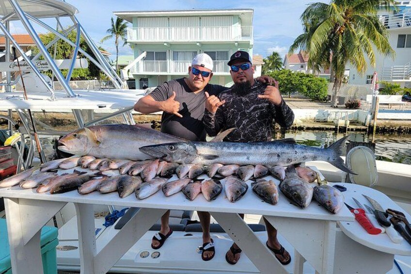 Two people on a boat with a large fish and several smaller fish on a table. 3