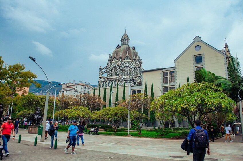 A plaza with people walking, a building with intricate architecture, and greenery. 2