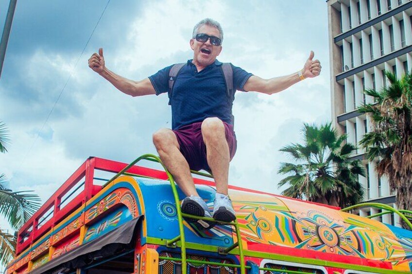 A man standing on a colorful bus with his arms outstretched. 1