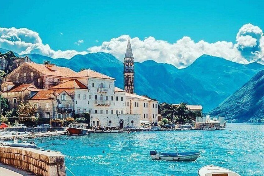A coastal town with a prominent church, boats docked along the harbor, and mountains in the background. 1