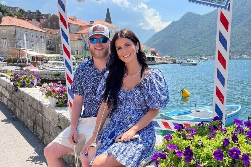 A couple sitting by a waterfront with a barber pole, boats, and mountains in the background. 2