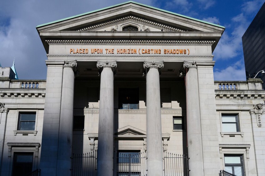 A neoclassical building with columns and a sign that reads "PLACED UPON THE HORIZON (CASTING SHADOWS)". 5