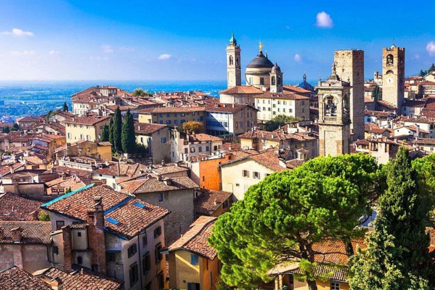 A historic town with red-tiled roofs, prominent towers, and a domed building. 1