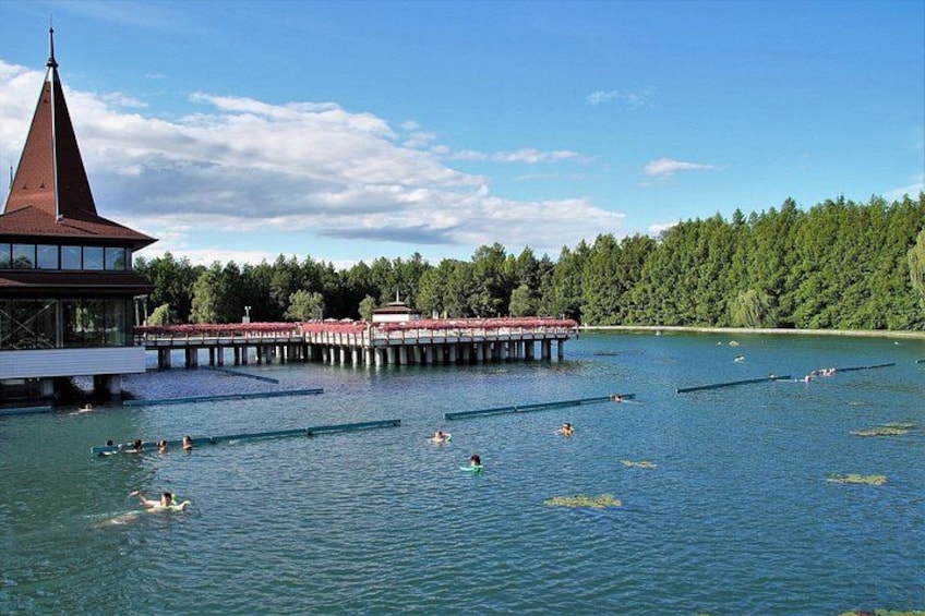 Un lago con nadadores, un muelle y un edificio de techo puntiagudo. 2