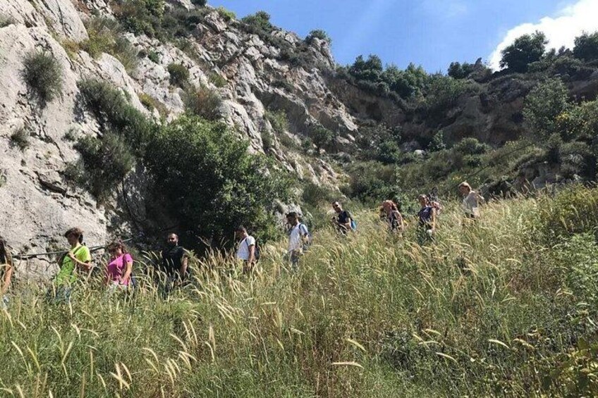 A group of people hiking on a grassy hillside with rocky terrain and sparse vegetation. 5