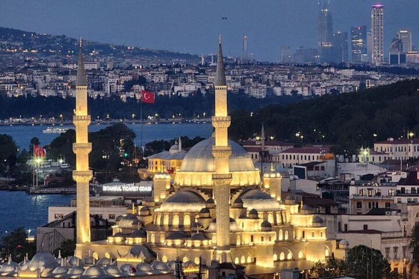 A cityscape with a prominent mosque featuring two minarets and a large dome, surrounded by urban buildings and a body of water. 1