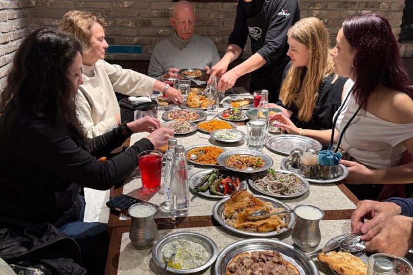 Un grupo de personas cenando alrededor de una mesa con diversos platos y bebidas. 3
